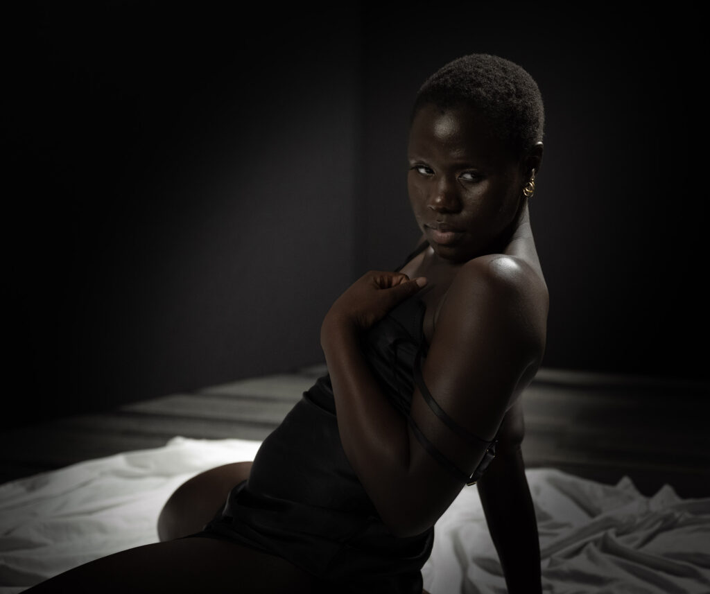 intimate portrait of African American woman in black lingerie posing on white sheet