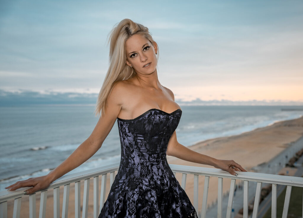 intimate portrait of a blonde woman in white lingerie standing on a balcony overlooking the beach